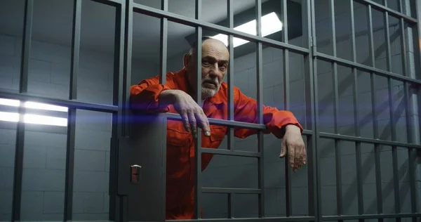 Starszy Więzień Pomarańczowym Mundurze Trzyma Ręce Metalowych Kratach Więzieniu Winny — Zdjęcie stockowe