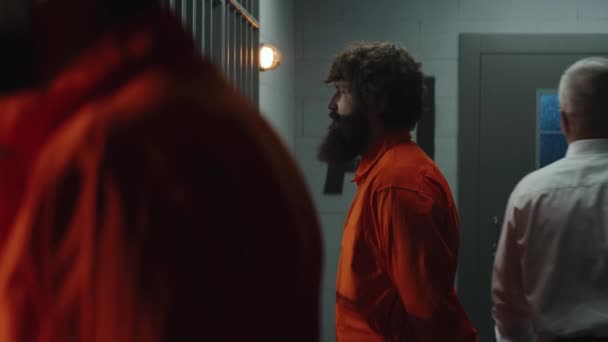 Turuncu Üniformalı Iki Mahkum Hapishane Hücrelerinin Önündeki Metal Parmaklıklara Bakıyor — Stok video