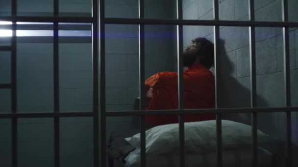 Häftling Orangefarbener Uniform Sitzt Auf Dem Bett Der Gefängniszelle Mit — Stockvideo