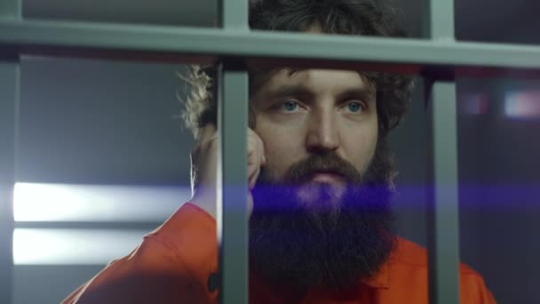 Заключенный Оранжевой Форме Стоит Металлическими Решетками Разговаривает Телефону Тюремной Камере — стоковое видео