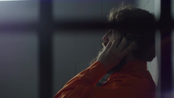 Заключенный Оранжевой Форме Сидит Кровати Разговаривает Телефону Тюремной Камере Преступник — стоковое видео