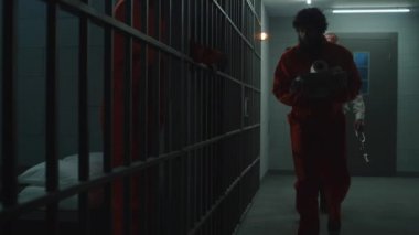 Gardiyan, turuncu üniformalı bir suçluyu hapishane hücresine götürüyor. Depresyondaki mahkum metal parmaklıklara bakıyor ve içeri giriyor. Mahkumlar gözaltı merkezinde veya cezaevinde hapis cezasına çarptırıldılar.