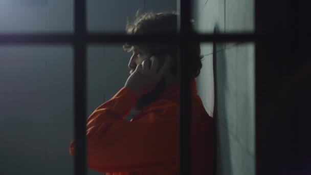 身穿橙色制服的囚犯躺在床上 在牢房里打电话 有罪的罪犯在狱中服刑 在拘留中心或教养所的囚犯 透过金属棒观看 — 图库视频影像