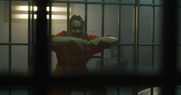 隣の収容所でオレンジの制服を着た囚人の狂気の女性が刑務所の独房のバーに飛び込む 女性犯罪者は懲役刑を言い渡される 拘置所だ 金属製のバーからの眺め — ストック写真