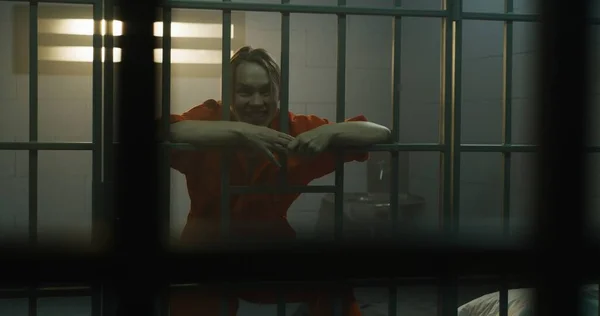 隣の収容所でオレンジの制服を着た囚人の狂気の女性が刑務所の独房のバーに飛び込む 女性犯罪者は懲役刑を言い渡される 拘置所だ 金属製のバーからの眺め — ストック写真
