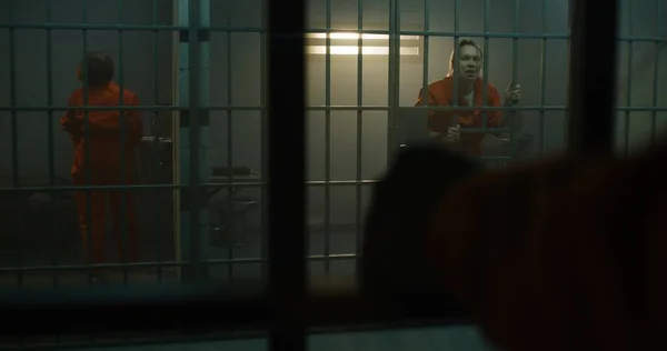 隣の収容所でオレンジの制服を着た囚人の狂気の女性が刑務所の独房の金属棒に飛び乗っている 女性は懲役刑を言い渡される 矯正施設内の犯罪者 司法制度 — ストック写真