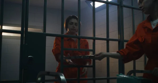 オレンジ色の制服を着た囚人は 食料提供のトロリーから刑務所の独房での女性犯罪者までディナーを提供する 女性犯罪者はベッドの上に座り 刑務所や拘置所で犯罪の刑期を務めます — ストック写真