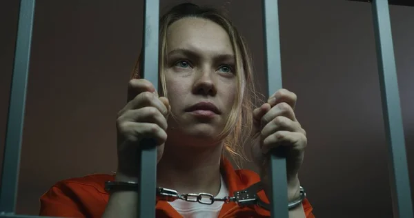 身穿橙色制服的女囚犯手持铁棍 戴着手铐站在牢房里 女犯人因在狱中犯罪而服刑 被关押在拘留中心的抑郁犯人 靠近点 — 图库照片