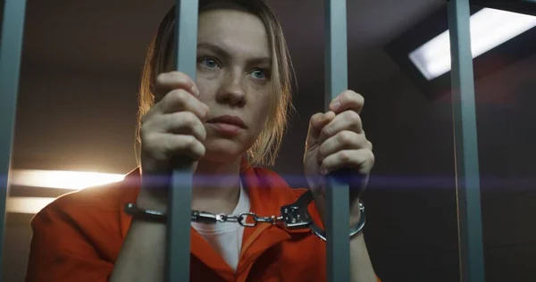 オレンジの制服を着た衝撃的な女性囚人は金属棒を持ち 手錠の独房に立っている 女性犯罪者は懲役刑を言い渡される 矯正施設の被収容者 肖像画 — ストック写真
