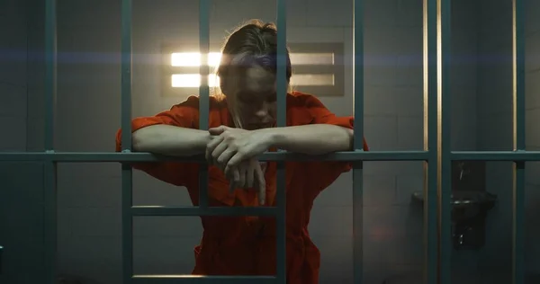 オレンジ色の制服を着た女性は金属の棒を手に持ち歩く刑務所の独房の中の窓を見る 女性は懲役刑を言い渡される 矯正施設の被収容者 — ストック写真