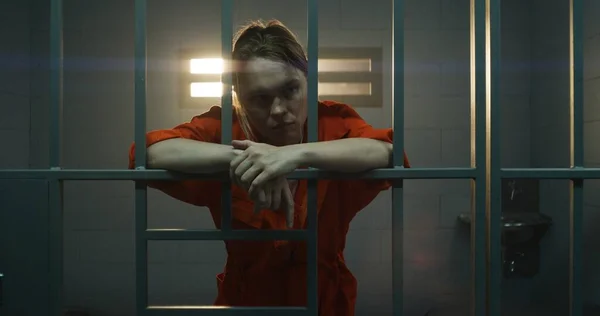 オレンジ色の制服を着た女性は金属の棒を手に持ち歩く刑務所の独房の中の窓を見る 女性は懲役刑を言い渡される 矯正施設の被収容者 — ストック写真