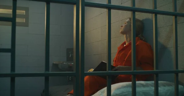 Vrouwelijke Gevangene Oranje Uniform Zit Bed Achter Metalen Tralies Leest — Stockfoto