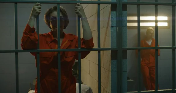 One Female Prisoner Orange Uniform Stands Metal Bars Another Sits — Stock Photo, Image