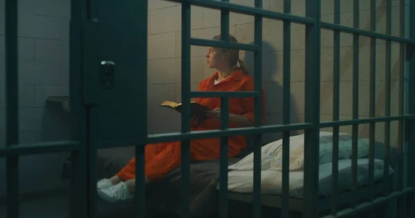 Kobieta Pomarańczowym Mundurze Siedzi Łóżku Metalowymi Kratami Czyta Biblię Więziennej — Zdjęcie stockowe