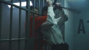 Cinematic shot of male prisoner strangling prison officer, taking keys and opening prison cell. Criminal in orange uniform escapes from jail. Editing action movie scene for TV screen. Movie making.
