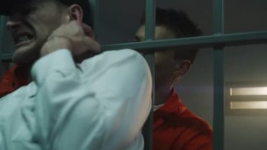 Male prisoner strangles prison officer, takes keys, opens prison cell. Criminal in orange uniform escapes from jail or correctional facility. Cinematic scene playback for action movie. Cinematography.