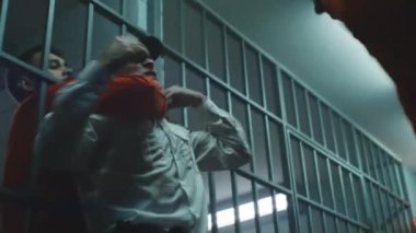 Prisoner in orange uniform fights with jailer. Another criminal strangles prison worker and removes handcuffs from cellmate. Escape from jail. Fighting in detention center or correctional facility.