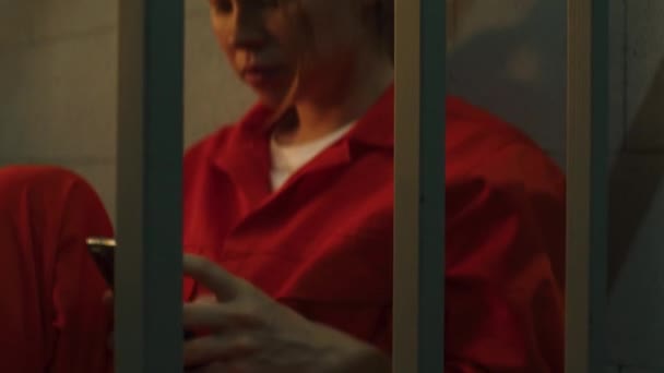 监狱工作人员给女囚犯打电话 身穿橙色制服的女犯人打电话来 坐在床上的牢房里 在监狱服刑 拘留中心或教养所 — 图库视频影像