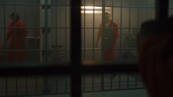 隣の収容所でオレンジの制服を着た囚人の狂気の女性が刑務所の独房の金属棒に飛び乗っている 女性は懲役刑を言い渡される 矯正施設内の犯罪者 司法制度 — ストック動画