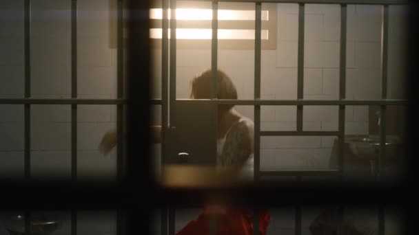 穿着橙色制服的女囚犯在牢房接受拳击和训练 女犯人因在狱中犯罪而服刑 拘留中心或教养所 透过金属棒观看 — 图库视频影像