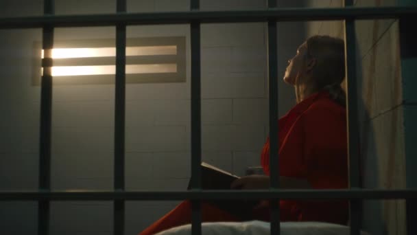 Vrouwelijke Gevangene Oranje Uniform Zit Bed Achter Metalen Tralies Leest — Stockvideo