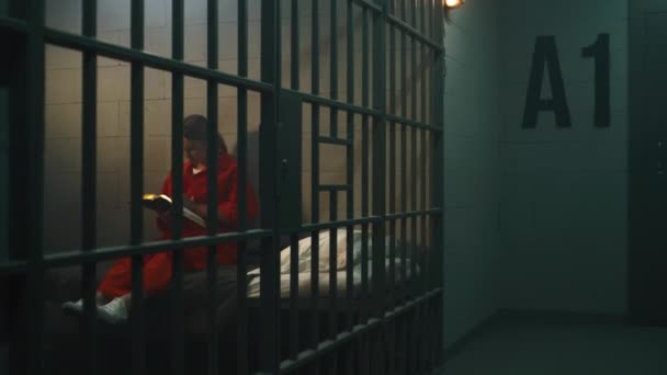 Vrouwelijke Gevangene Oranje Uniform Zit Het Bed Achter Tralies Leest — Stockvideo