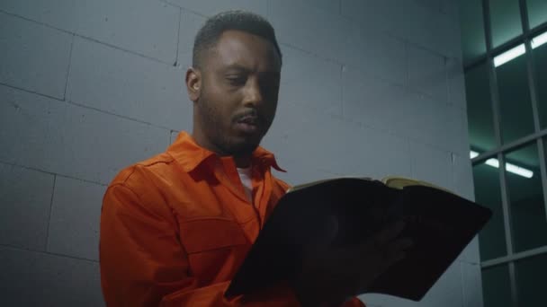 Africký Zajatec Oranžové Uniformě Sedí Vězeňské Cele Čte Bibli Mužský — Stock video