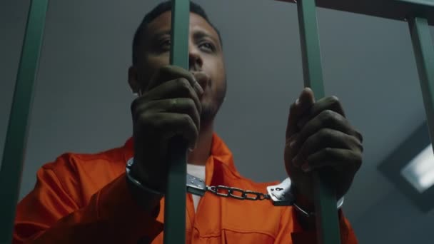 Afroamerikansk Man Orange Uniform Håller Händerna Handbojor Fängelsets Cellstänger Deprimerad — Stockvideo