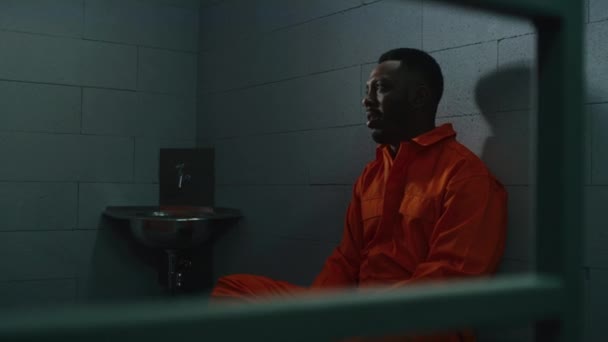 アフリカ系アメリカ人はベッドに座り 刑務所で犯罪者と話す 補正施設でオレンジ色の制服を着た2人の囚人 囚人は拘置所の犯罪のための投獄条件を提供する — ストック動画