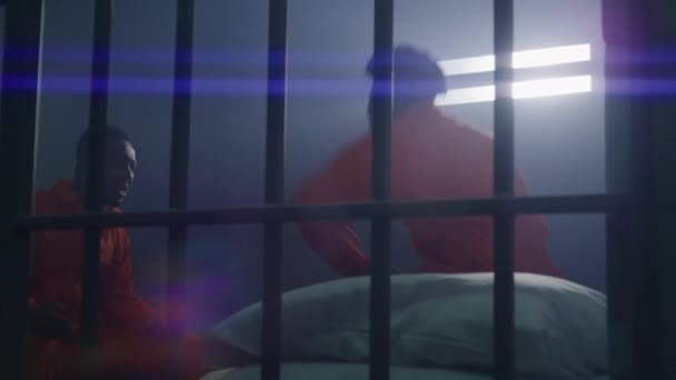 两个身穿橙色制服的囚犯坐在监狱床上 谈情说爱 男性罪犯在牢房里推挤室友和打架 囚犯因在惩教所犯罪而服刑 — 图库视频影像