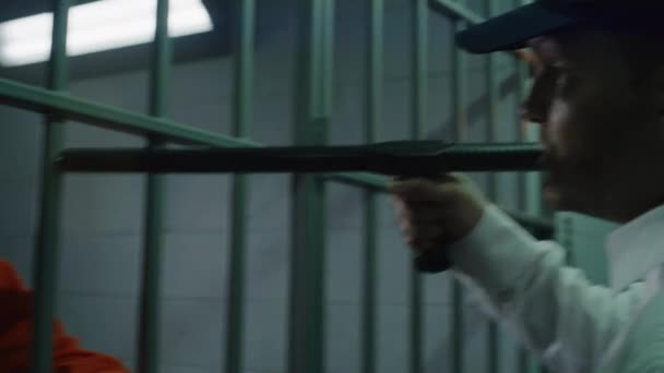 バトンが付いている保安官は 刑務所の監獄の前に立っており いじめの囚人です 抑圧されたアフリカ系アメリカ人男性は 拘留センターで投獄期間を過ごしている 補正施設でオレンジ色のユニフォームの殺人者 — ストック動画