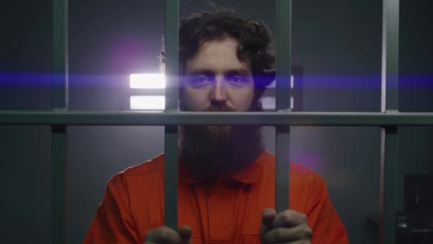 オレンジ色の制服の囚人は 金属製の棒を保持し 手錠で刑務所の監房に立って カメラを見ています 刑務所では刑務所で有罪判決が下される 修正施設で疲れた囚人 ポートレイト — ストック動画