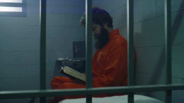 Manlig Fånge Orange Uniform Sitter Sängen Läser Bibeln Tittar Spärrade — Stockvideo