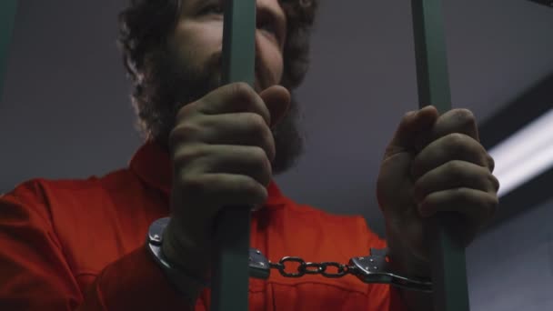 Homem Prisioneiro Uniforme Laranja Segura Barras Metal Com Mãos Algemadas — Vídeo de Stock
