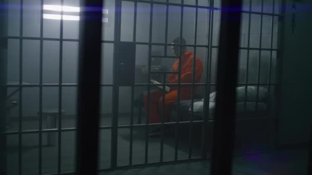 Afrikansk Amerikansk Fånge Orange Uniform Sitter Sängen Läser Bibeln Fängelsecell — Stockvideo
