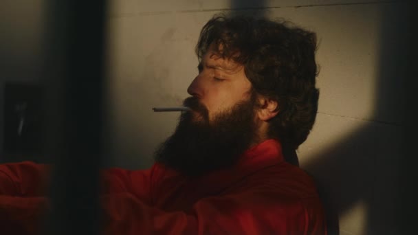 Задумчивый Заключенный Мужчина Оранжевой Форме Сидит Кровати Зажигает Сигарету Зажигалкой — стоковое видео