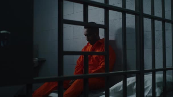 Schuldige Afro Amerikaanse Man Oranje Uniform Zit Het Gevangenisbed Denkt — Stockvideo
