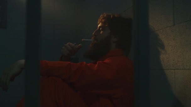 Deprimerad Manlig Fånge Orange Uniform Sitter Sängen Röker Cigarett Fängelsecell — Stockvideo