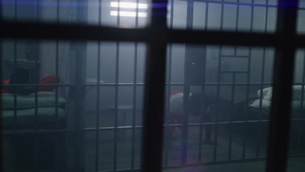 Turuncu Üniformalı Bir Mahkum Yatakta Yatıyor Diğeri Şınav Çekiyor Hücrede — Stok video