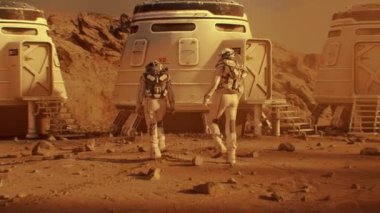 Uzay elbiseli iki astronot Mars 'taki araştırma istasyonuna, koloniye ya da bilimsel üsse doğru yürüyorlar. Kızıl Gezegen 'de insanlı uzay görevleri. Gelecekçi kolonileşme ve uzay keşfi kavramı.