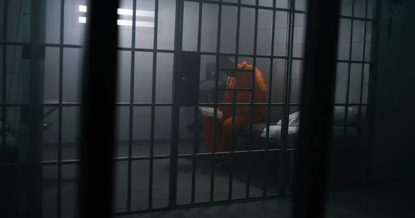 Africký Zajatec Oranžové Uniformě Sedí Posteli Čte Bibli Vězeňské Cele — Stock fotografie