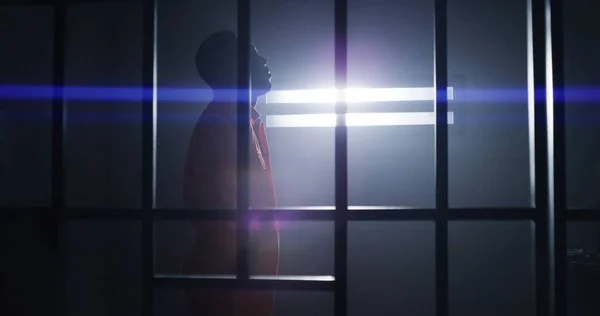 オレンジ色の制服を着た抑圧されたアフリカ系アメリカ人は 刑務所のベッドから立ち 刑務所の監房を歩き 野蛮な窓を見ている 囚人は投獄期間を定めている 暗い矯正施設での殺人者 — ストック写真