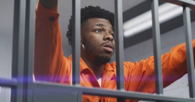 Turuncu üniformalı üzgün Afro-Amerikan adam hapishane parmaklıklarına yaslanıyor ve boynu yoğuruyor. Depresyondaki mahkum hapiste hapis yatıyor. Islah evinde ya da gözaltı merkezinde katil.