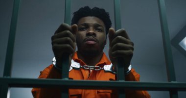 Turuncu üniformalı Afro-Amerikan adam hapishane parmaklıklarında elleri kelepçeli. Depresyondaki katil hapiste hapis yatıyor. Islah evinde ya da gözaltı merkezinde suçlu..