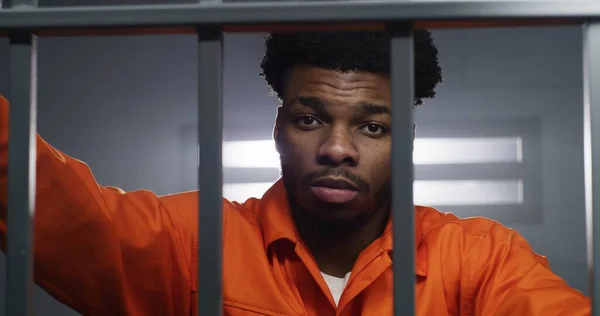 Afroamerikansk Mand Orange Uniform Ser Kamera Knæhals Fængselscelle Fangen Afsoner - Stock-foto