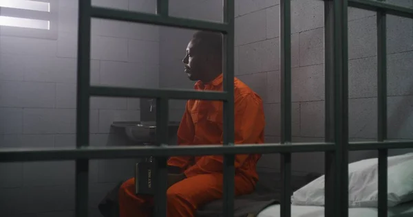 Prisioneiro Afro Americano Uniforme Laranja Senta Cama Atrás Das Grades — Fotografia de Stock