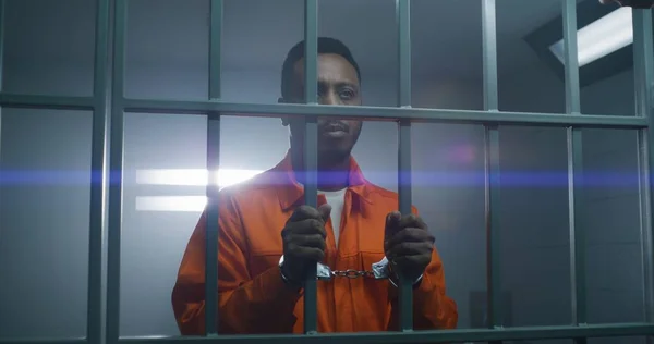 Afroamerykanin Pomarańczowym Mundurze Trzyma Ręce Kajdankach Więziennych Kratach Patrzy Kamerę — Zdjęcie stockowe