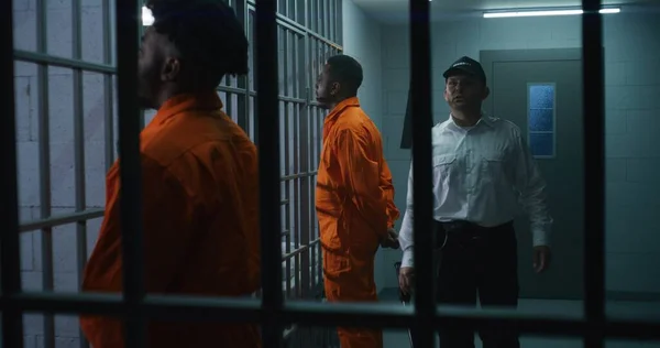 警察のバトンを持つ刑務所の従業員は刑務所の廊下を歩き 囚人をいじめます アフリカ系アメリカ人犯罪者は背後に手で携帯する 拘置所で有罪判決を受けた殺人者 — ストック写真