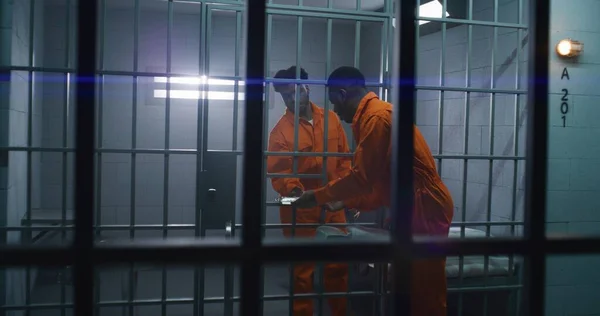 オレンジ色の制服を着た男は トロリーに仕えることから刑務所の囚人に食べ物を与える 抑圧された犯罪者はベッドに座り 夕食を食べ 犯罪のための投獄期間を提供します 刑務所 矯正施設について — ストック写真