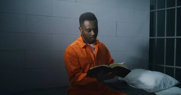 Africký Zajatec Oranžové Uniformě Sedí Vězeňské Cele Čte Bibli Mužský — Stock fotografie